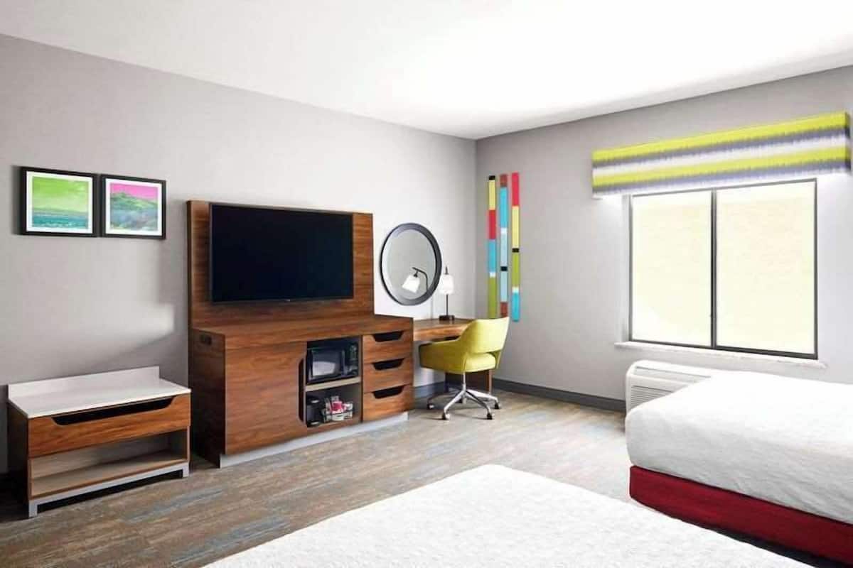 A modern hotel room with a flat-screen TV, a desk with a chair, a bed, and a large window.