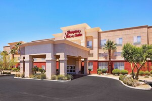 Edificio de Hampton Inn Suites con entrada despejada, palmeras y jardines bien cuidados.