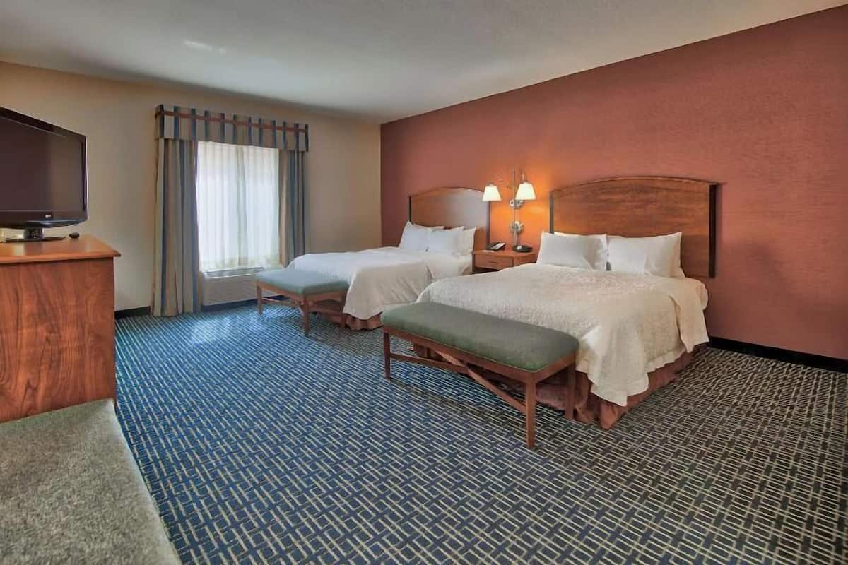 A hotel room with two beds, a TV, a desk, and a window with curtains.