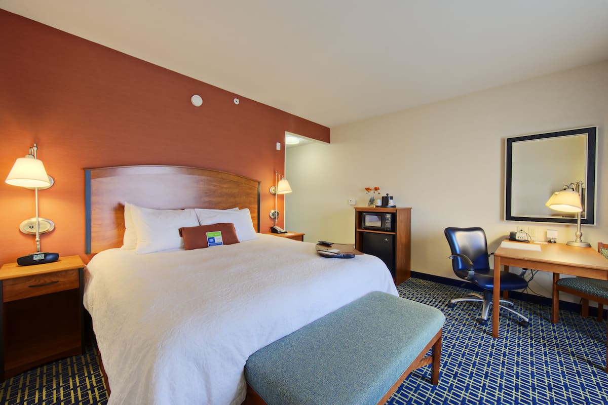 A hotel room with a large bed, bedside lamps, a desk, a chair, and a mirror.