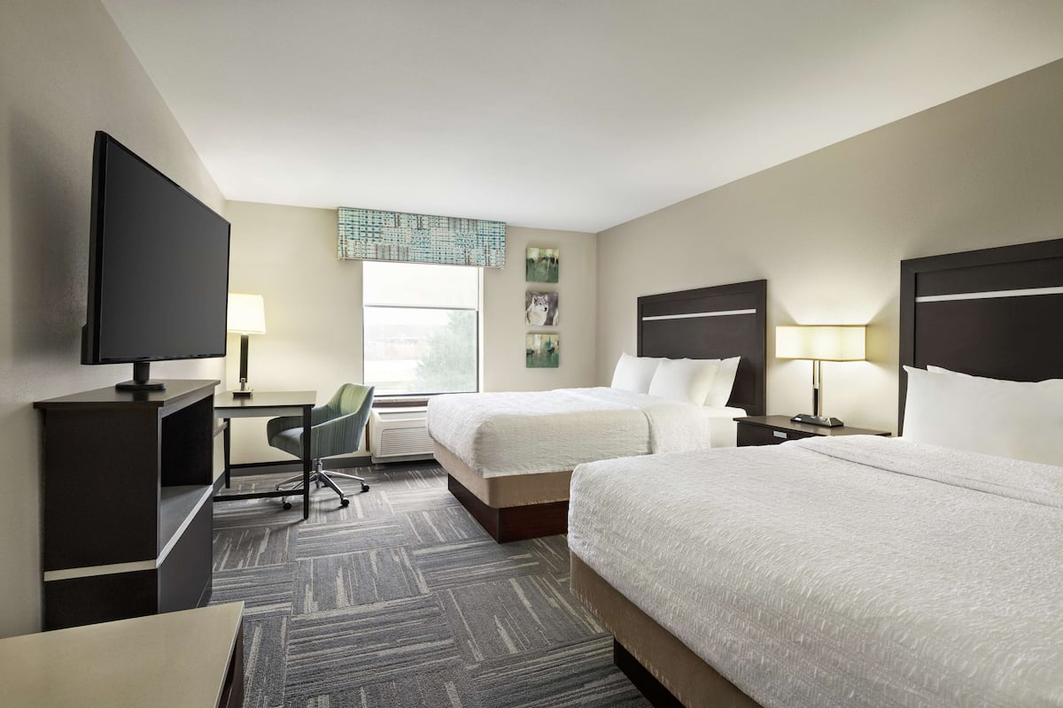 A hotel room with two beds, a desk with a chair, a TV, and a window with a view.