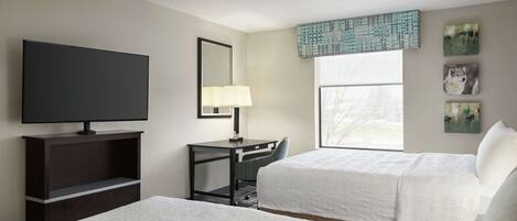 A hotel room with two beds, a desk, a TV, and artwork on the wall.