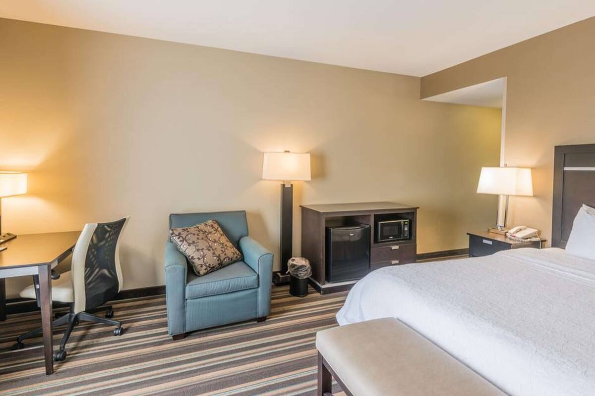 A hotel room with a bed, a desk with a chair, a small kitchenette, and two bedside lamps.
