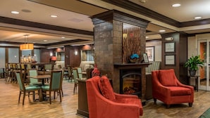 A lobby with a fireplace, red armchairs, a dining area with tables and chairs, and a reception desk.