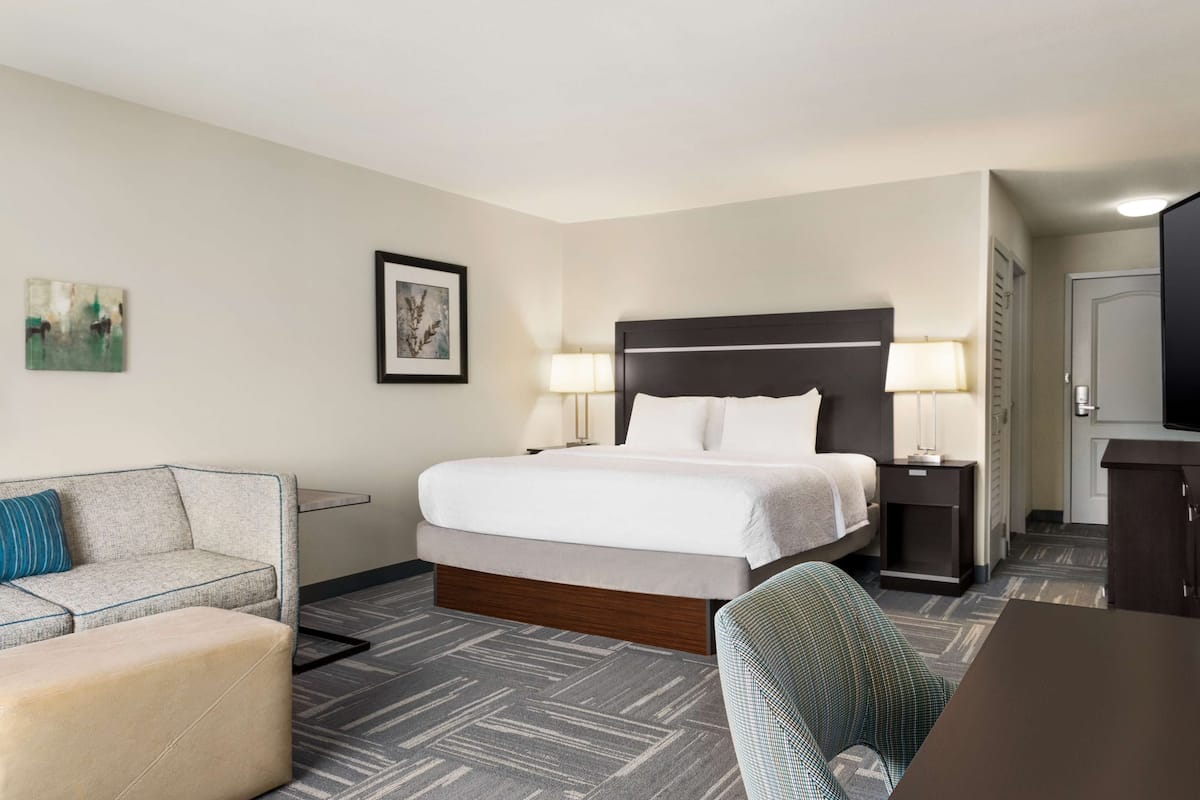 A hotel room with a bed, a desk, a chair, a sofa, and two lamps.