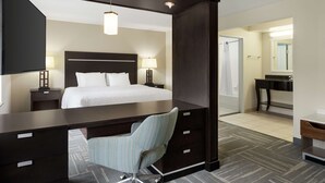 A hotel room with a bed, desk, chair, and a bathroom visible through an open door.