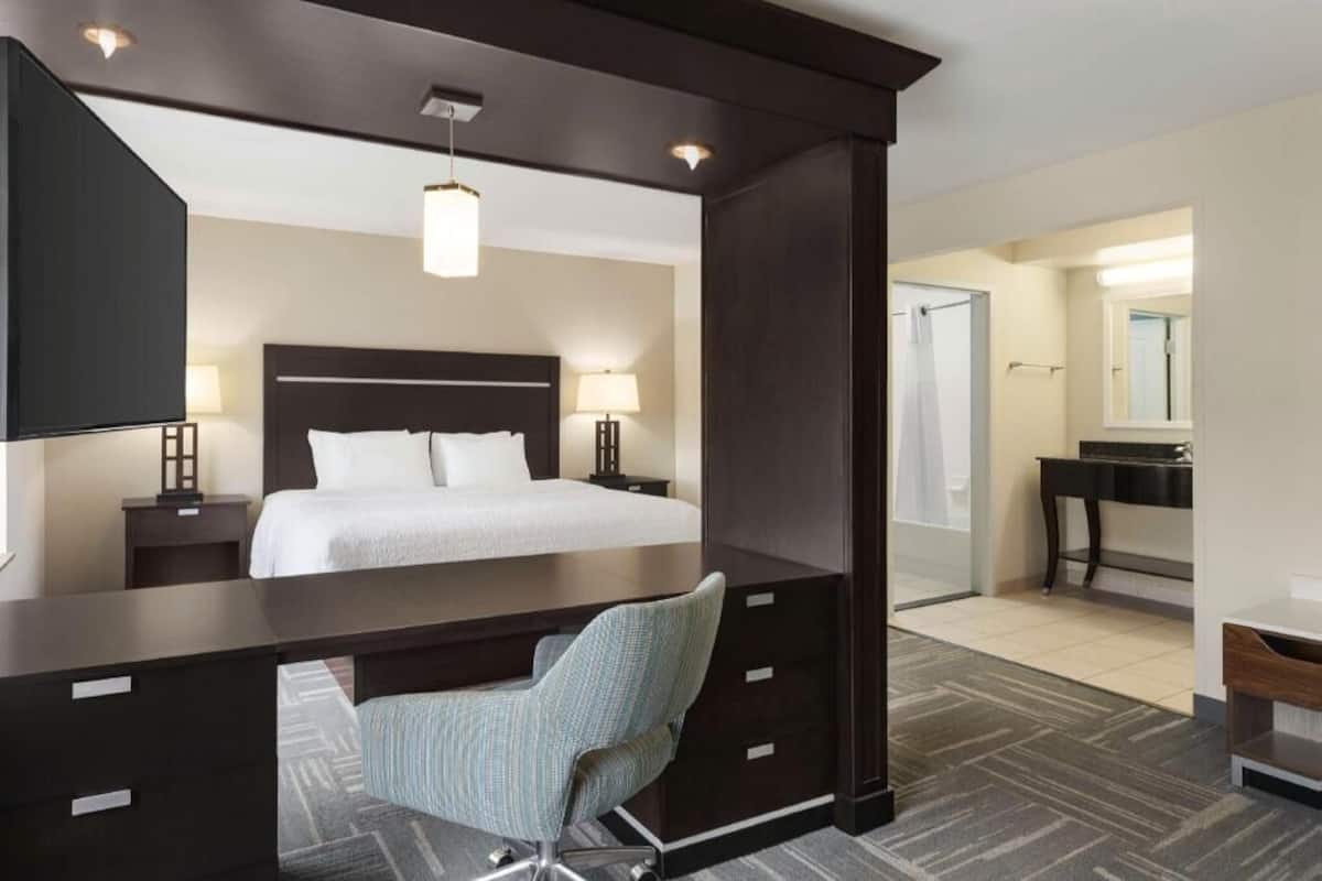 A hotel room with a bed, desk, chair, bedside lamps, and a mirror.