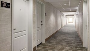 A hotel hallway with white doors, numbered room signs, and a carpeted floor.