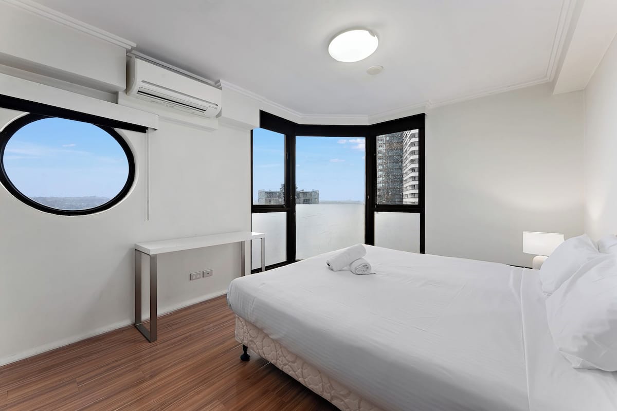A modern hotel room with a large bed, a round window, and a view of the cityscape.