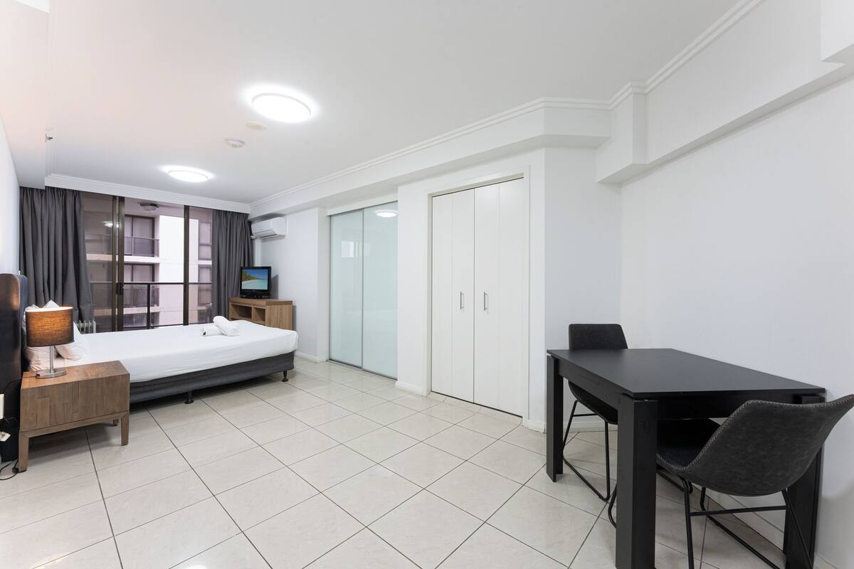 A modern hotel room with a bed, a desk with a chair, a TV, and a wardrobe.