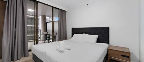 A hotel room with a large bed, a bedside table, a chair, and a view of the outside.