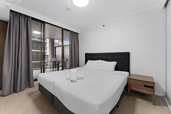 Habitación de hotel con una cama grande, una mesita de noche, una silla y vistas al exterior.
