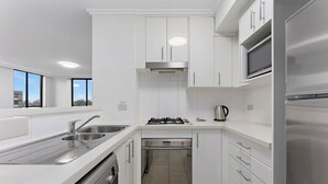 A modern kitchen with white cabinetry, stainless steel appliances, a dishwasher, and a built-in oven. - Fiori Apartments (Parramatta)