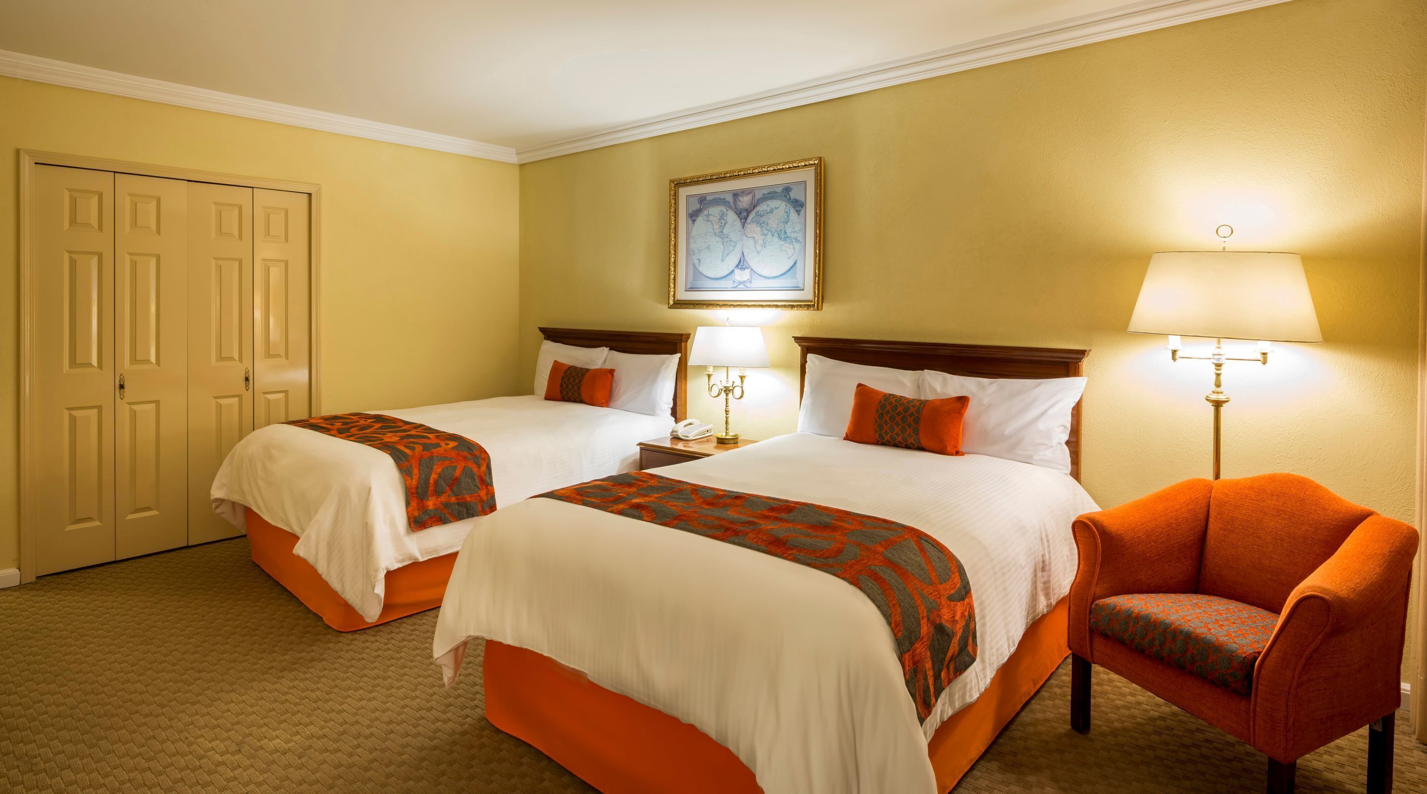 A hotel room with two beds, a chair, a lamp, and a painting on the wall.
