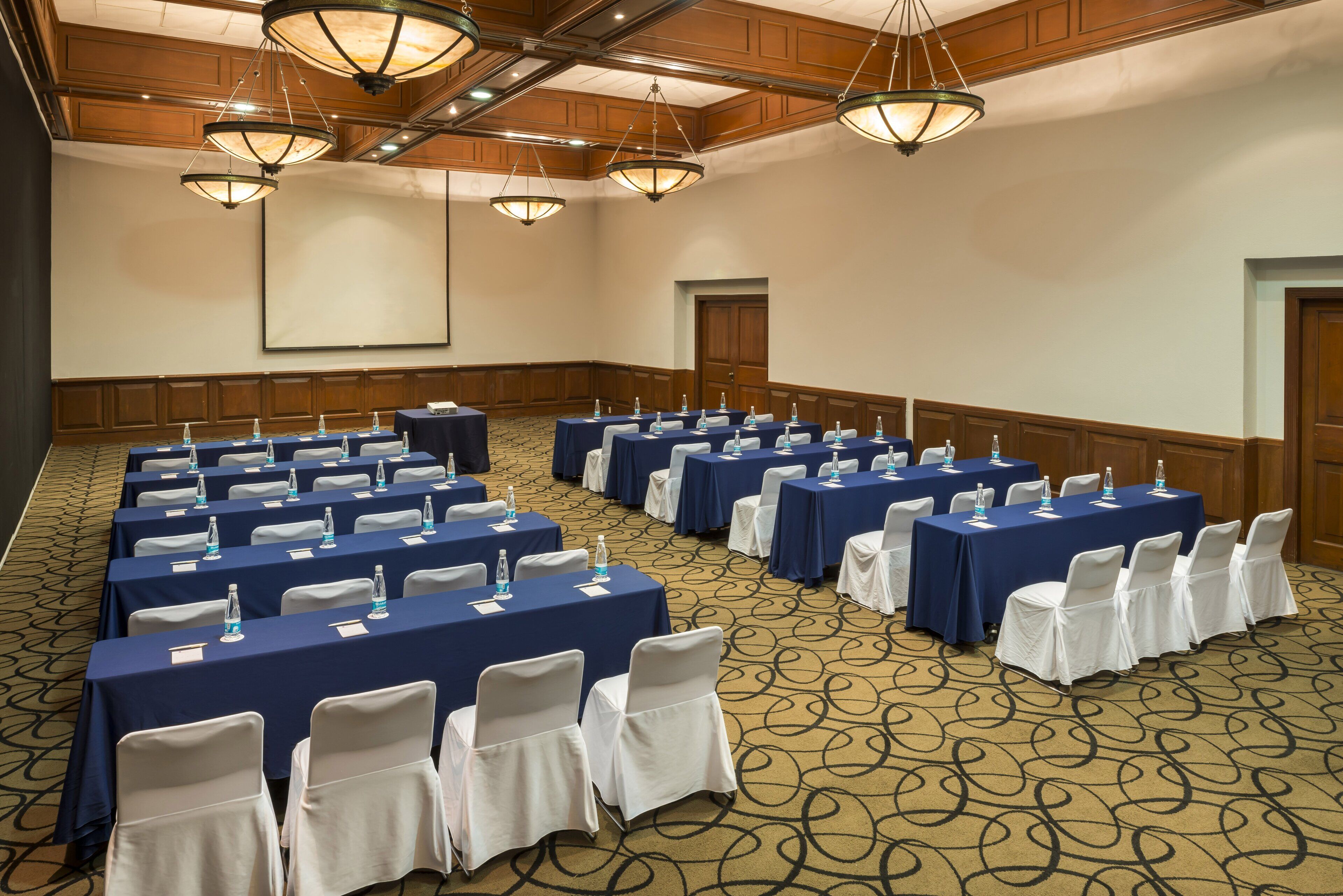 Un salón de conferencias con mesas, sillas y una pantalla de proyector.