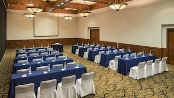 Une salle de conférence avec des rangées de tables, de chaises et un écran de projection.