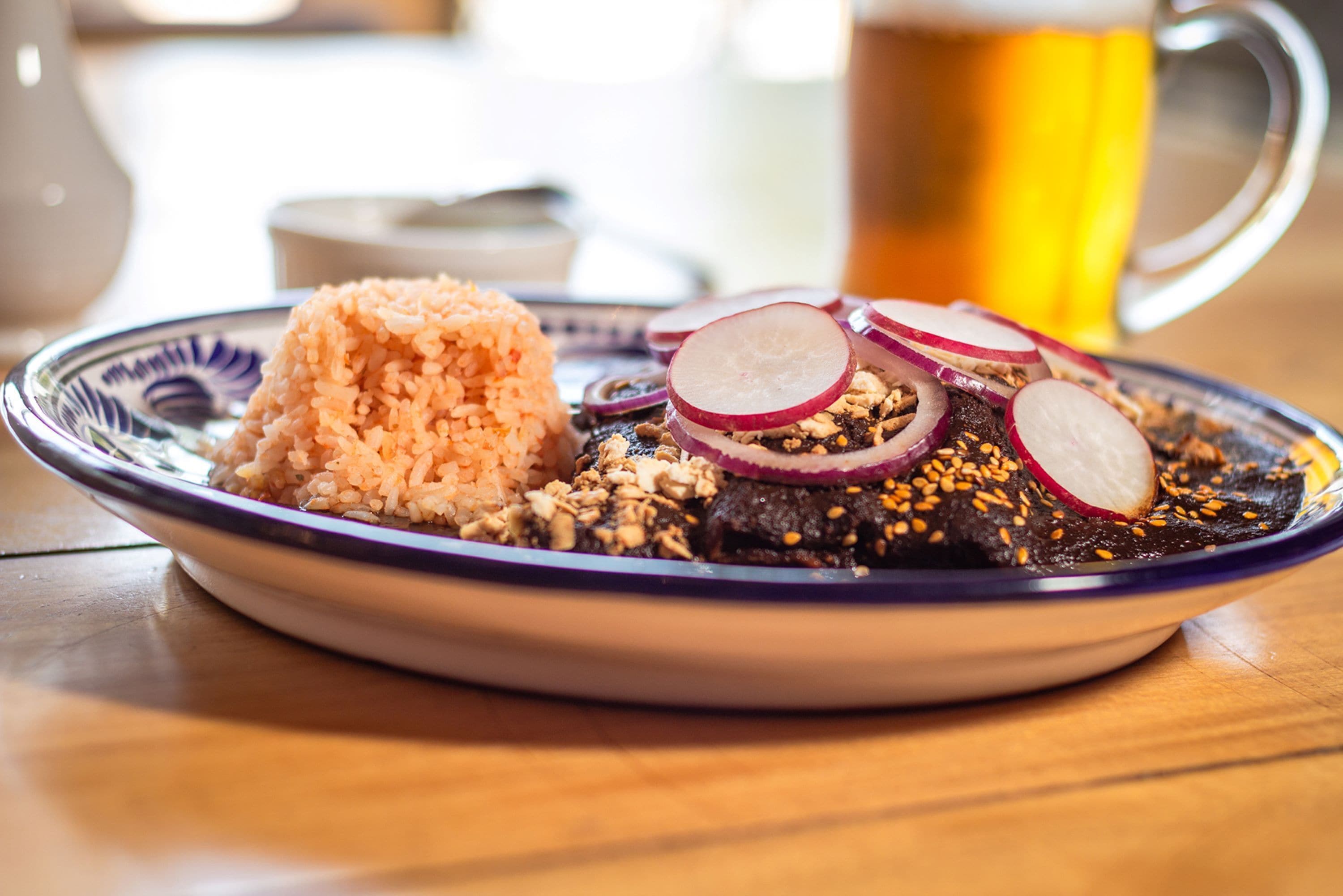 A plate of food with rice, beans, and sliced radishes, accompanied by a mug of beer.