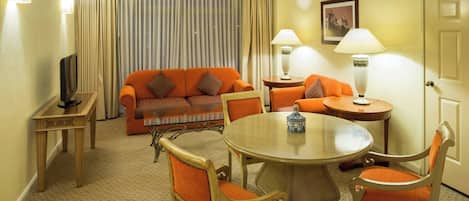 A hotel room with a sofa, two armchairs, a coffee table, a TV, and lamps.