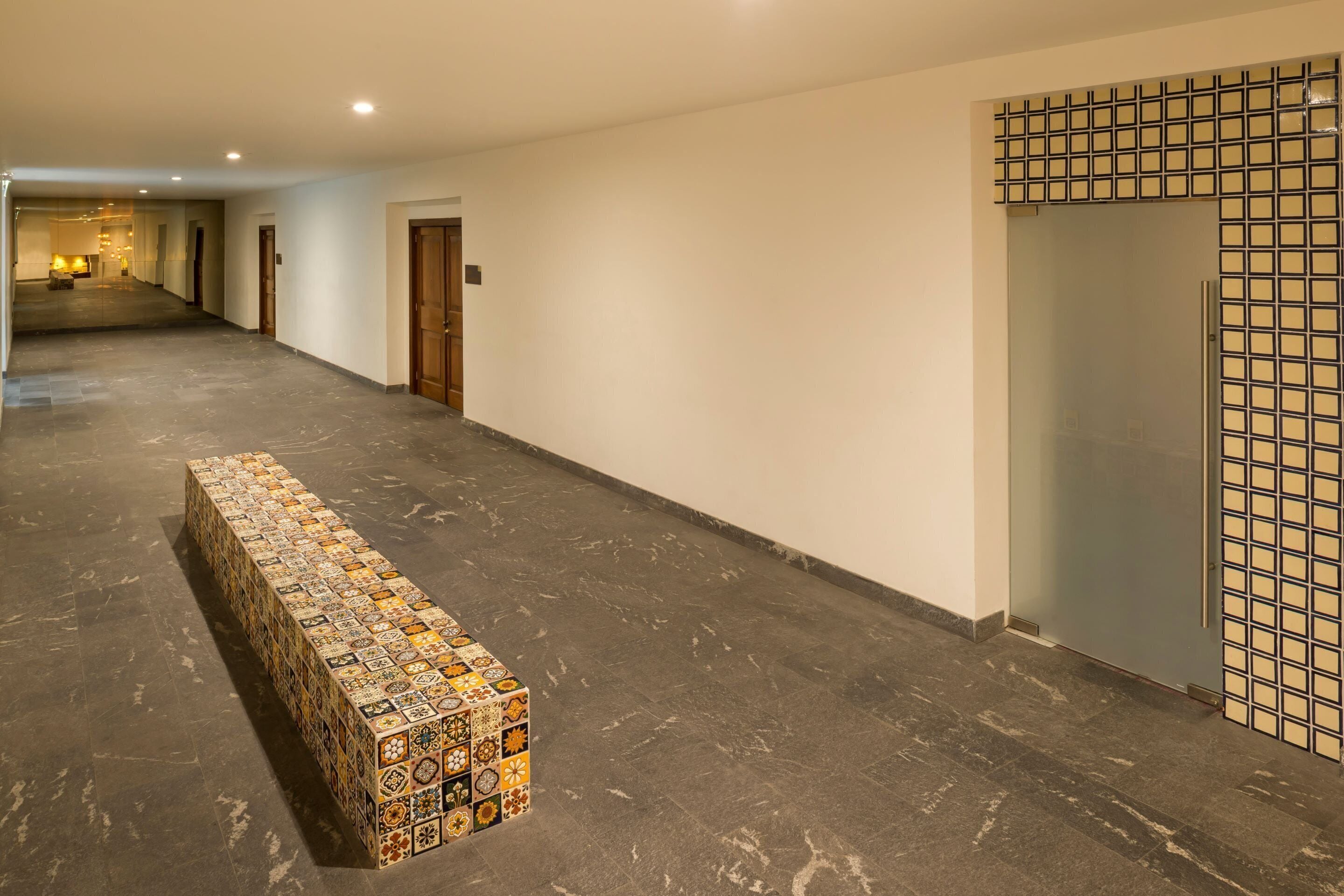 A long hallway with a tiled bench, doors, and a patterned wall.