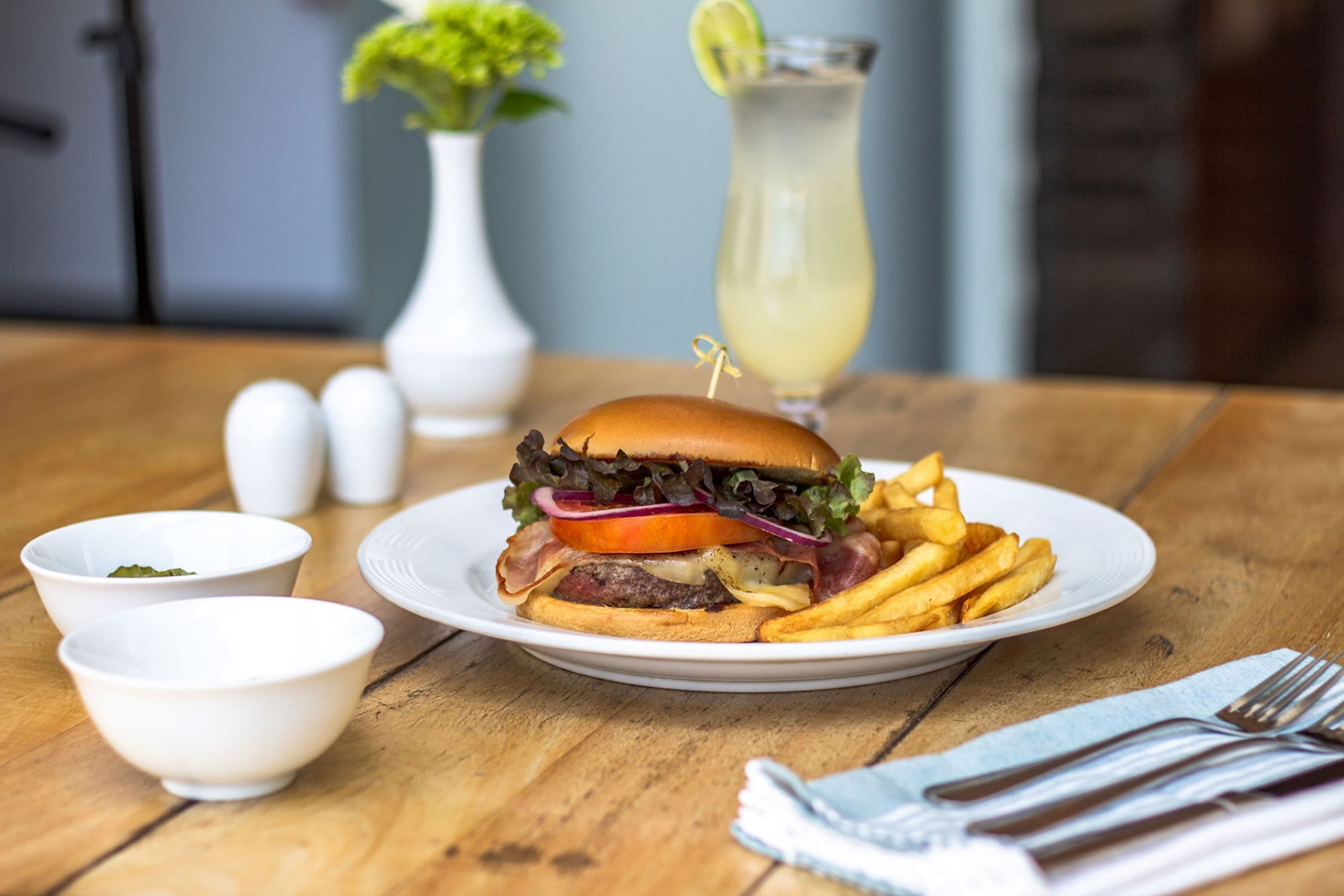 Comida con una hamburguesa, papas fritas y una bebida sobre una mesa de madera.