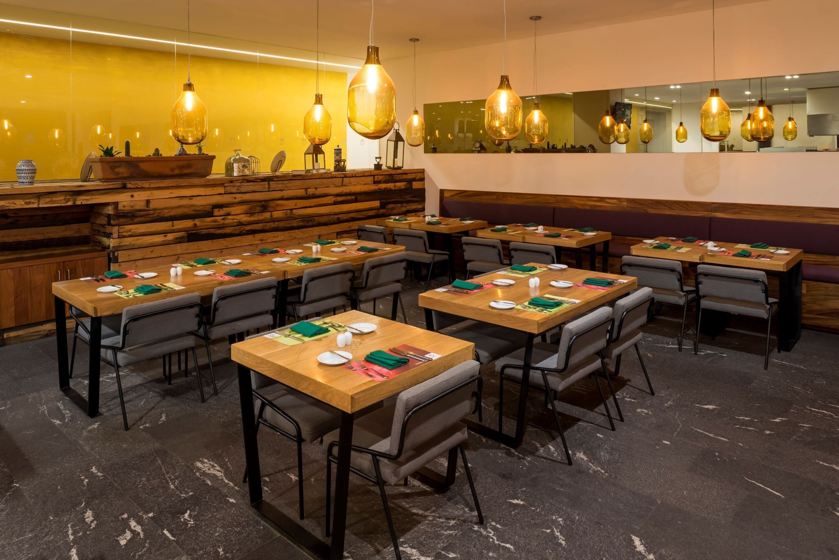 A restaurant with wooden tables and chairs, a counter with a rustic design, and hanging pendant lights.
