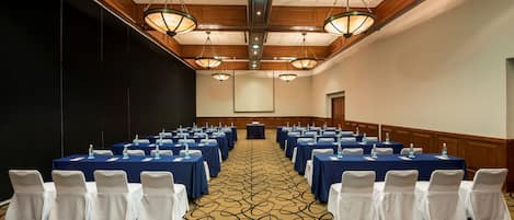 A conference room with rows of tables and chairs, equipped with water bottles, in a room with wooden paneling and patterned carpet.