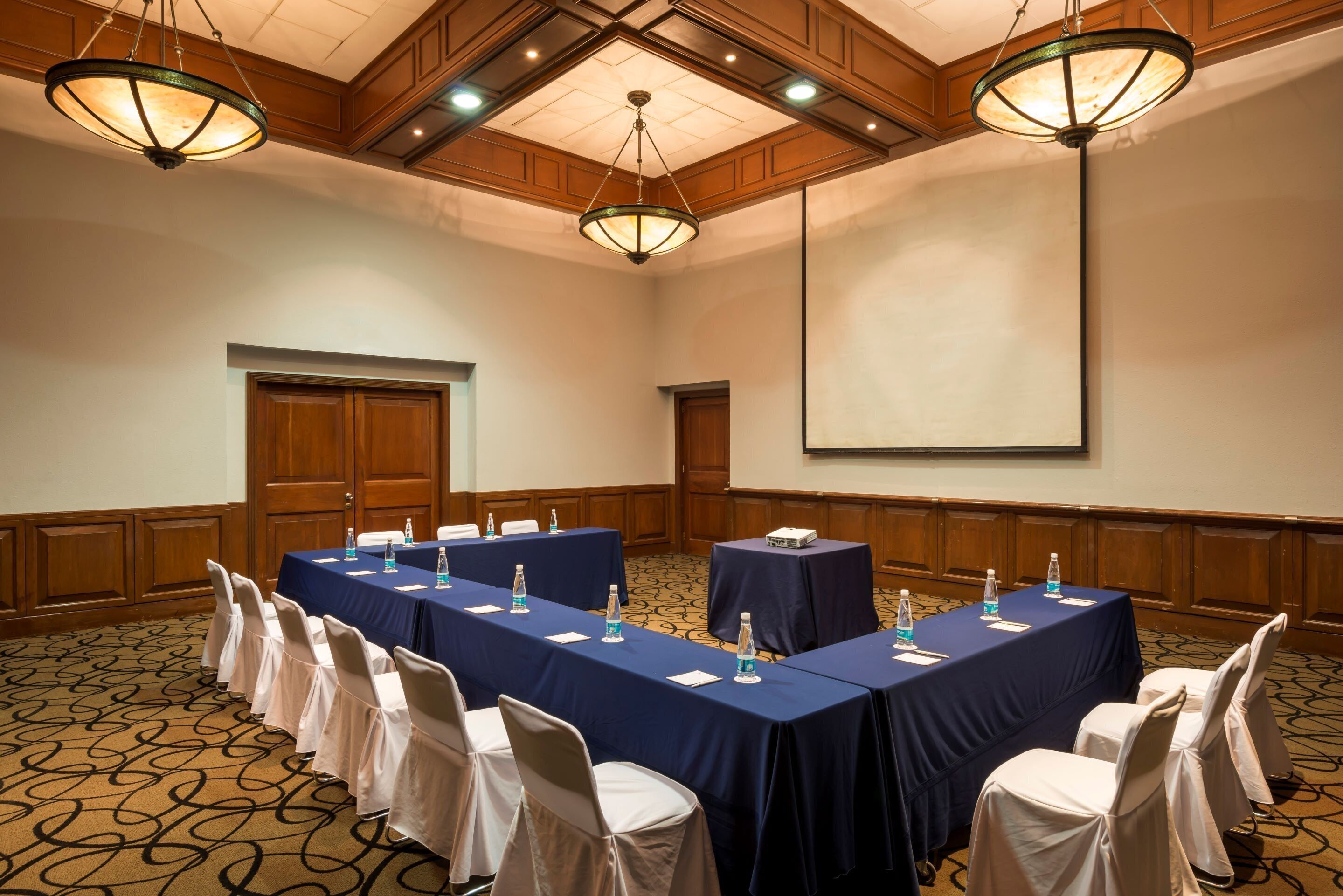 A conference room with long tables, chairs, and a projector screen.