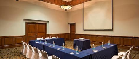 A conference room with long tables, chairs, and a projector screen.