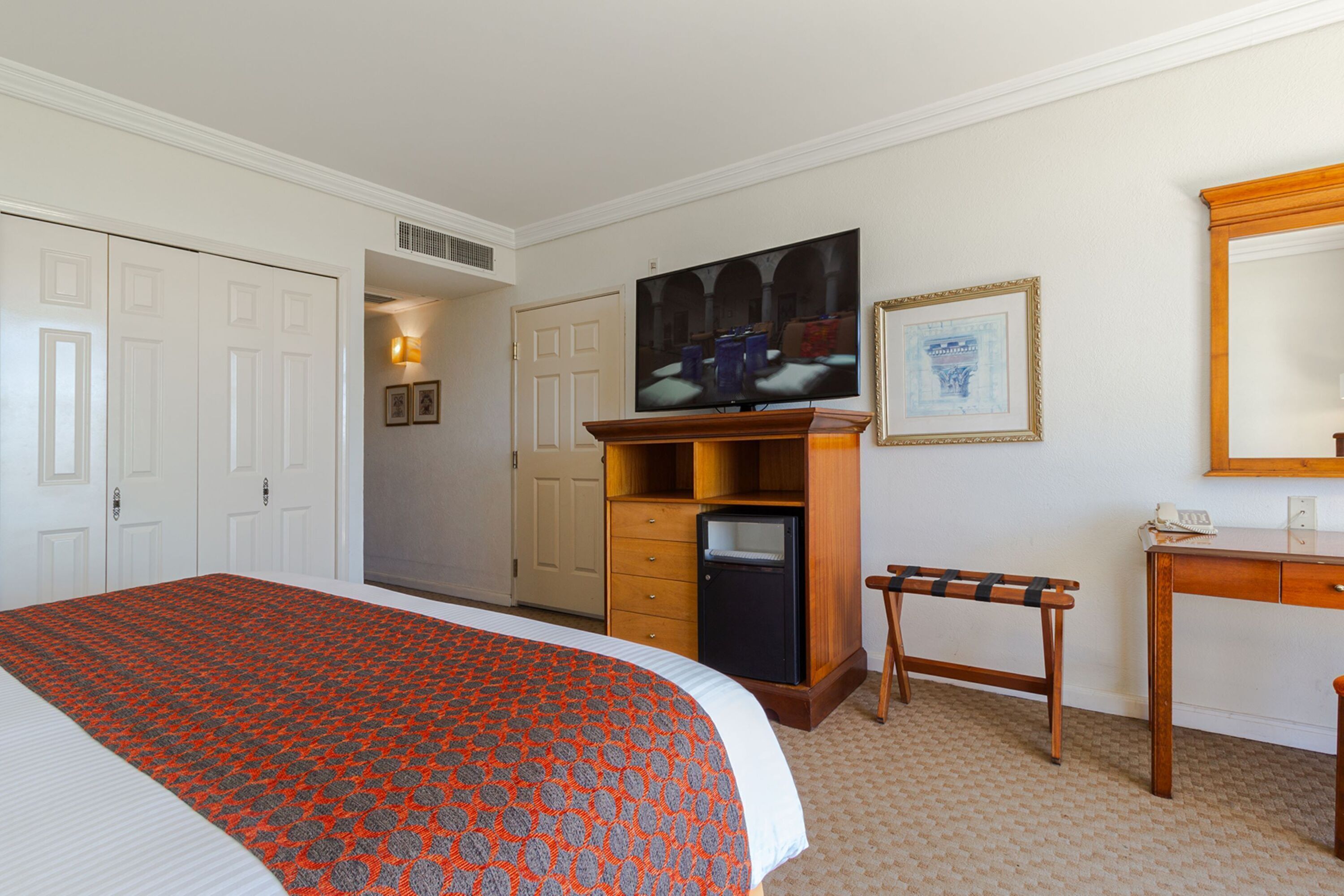 A hotel room with a large bed, a television, a desk, and a wardrobe.