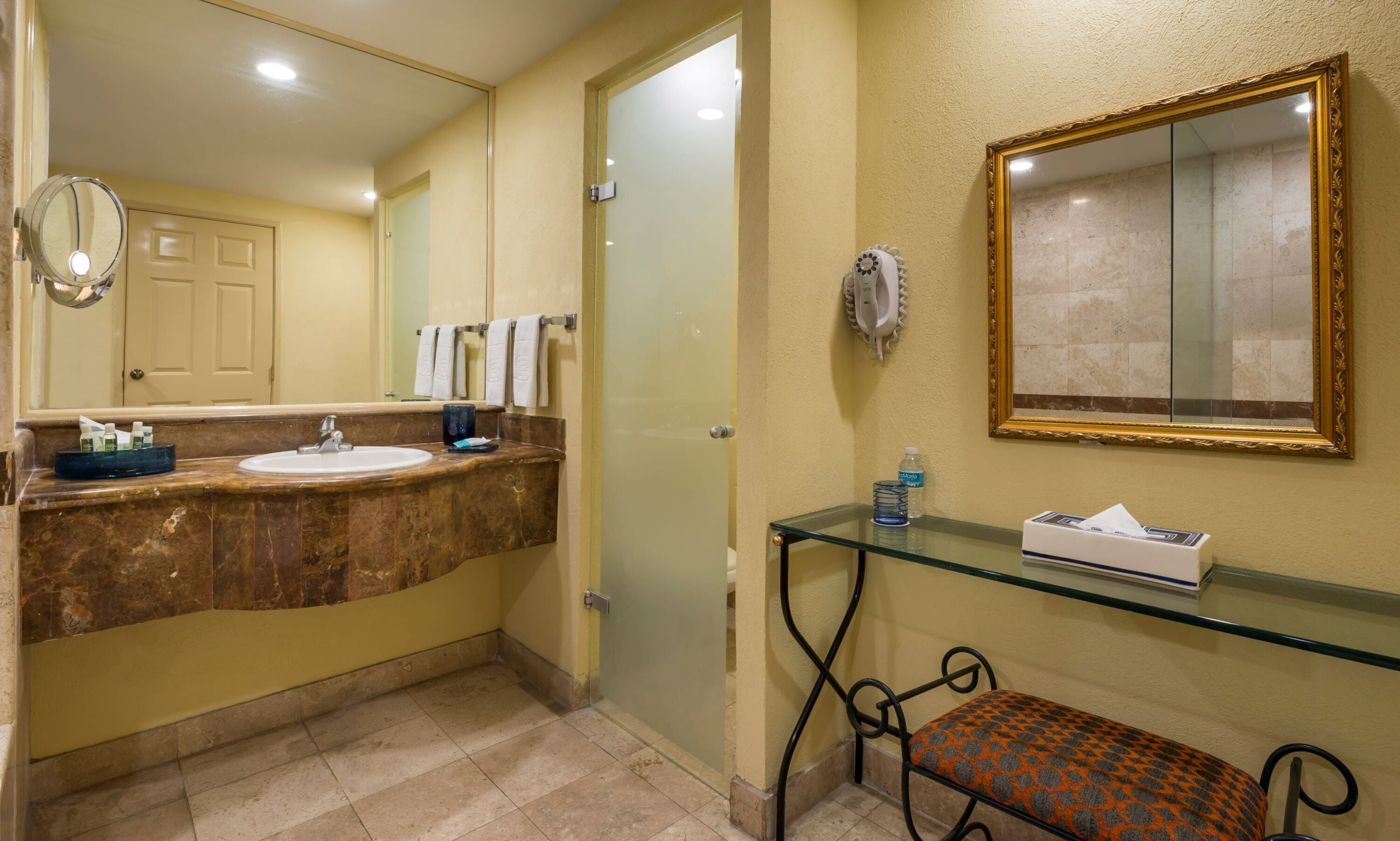 Une salle de bain avec un lavabo en marbre, un banc en verre, un miroir et une porte en verre.