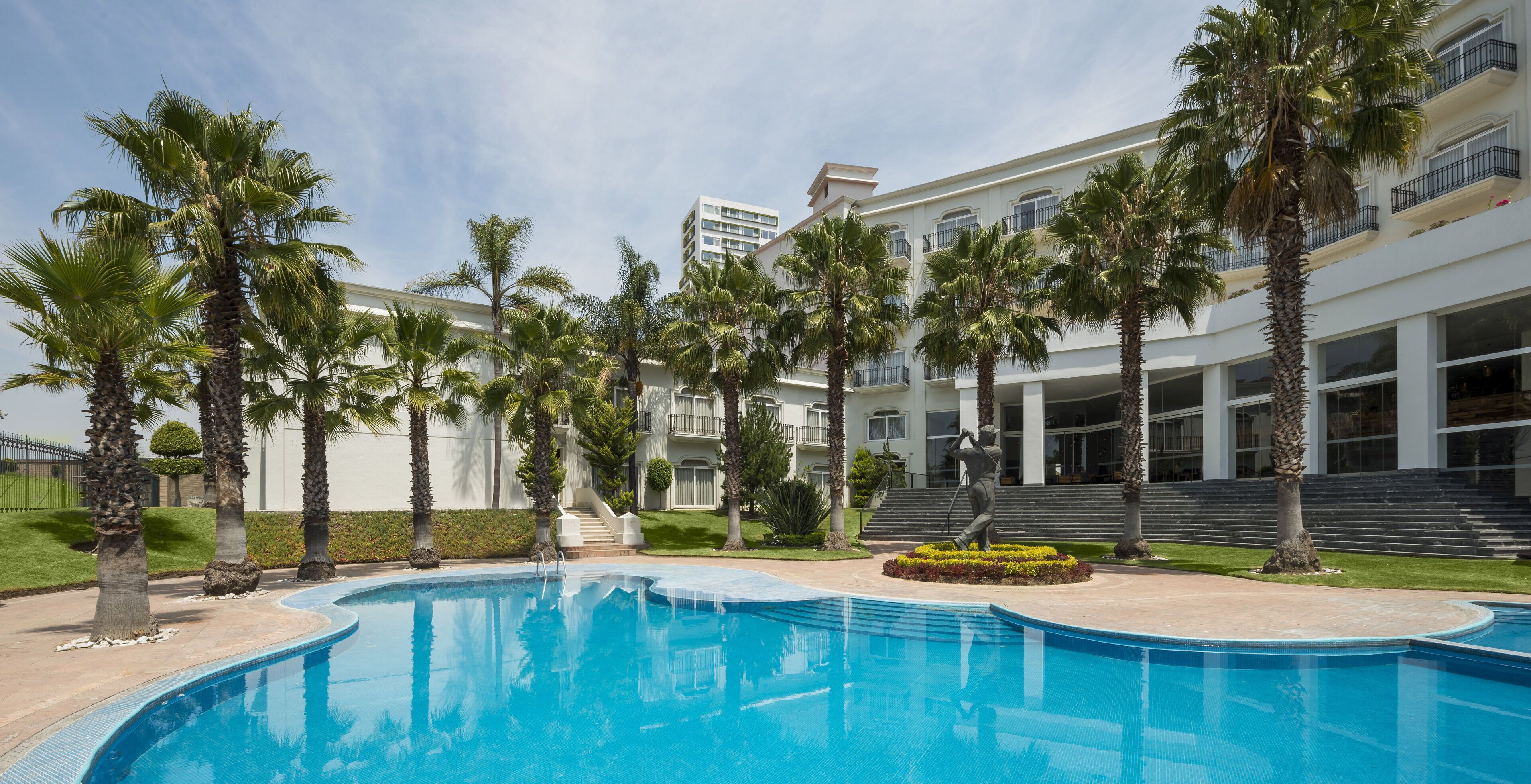 A swimming pool surrounded by palm trees and a multi-story building with balconies.
