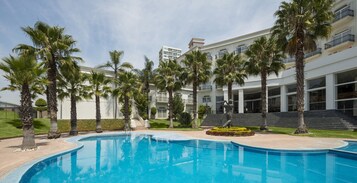 Una piscina rodeada de palmeras y un edificio de varios pisos con balcones.