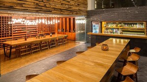 A bar area with wooden tables and chairs, a wine rack, and a bar counter with bottles. - Camino Real Puebla Angelopolis (San Andrés Cholula)