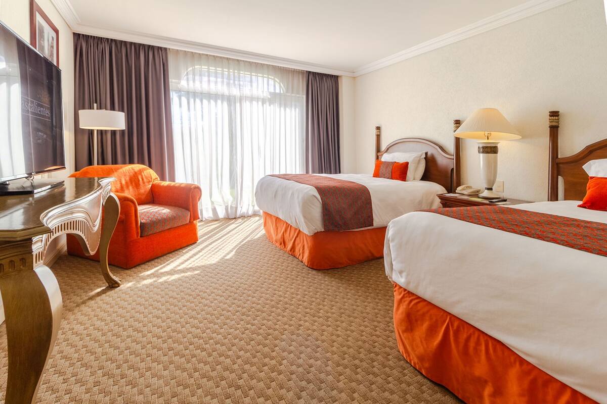 Une chambre d’hôtel avec deux lits, un bureau, une chaise, une télévision et une lampe.