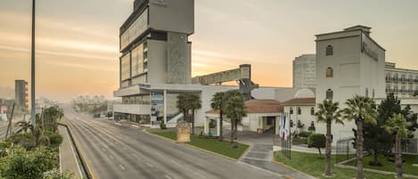 A modern hotel with a prominent tower, a covered walkway, and a well-maintained lawn with palm trees.