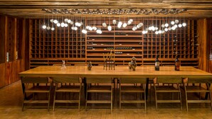 A wooden wine cellar with a long table and chairs, surrounded by wine racks. - Camino Real Puebla Angelopolis (San Andrés Cholula)