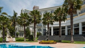 A pool area with palm trees, a statue, and a modern building with multiple floors and balconies. - Camino Real Puebla Angelopolis (San Andrés Cholula)
