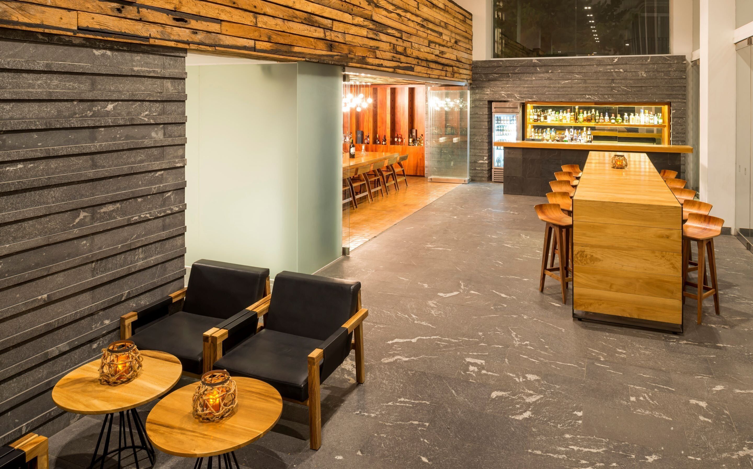 A bar area with wooden bar stools, a long counter, and a seating area with round tables and chairs.