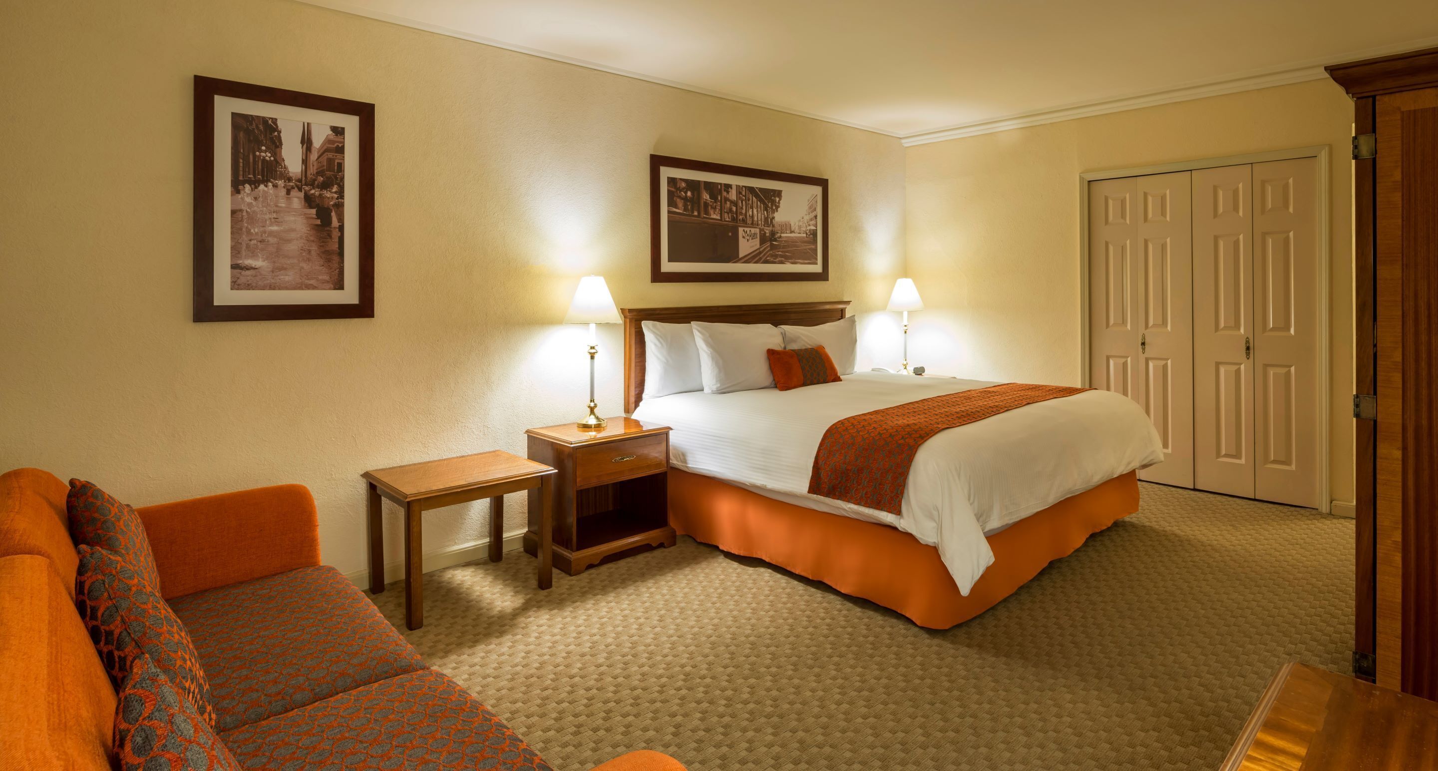 A hotel room with a large bed, two bedside tables with lamps, a sofa, and a door.