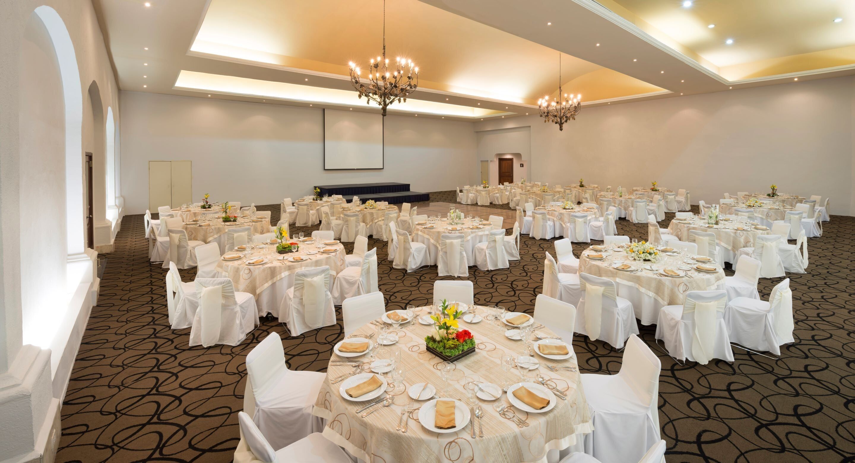 Une grande salle de banquet avec des tables rondes, des chaises blanches et des lustres.