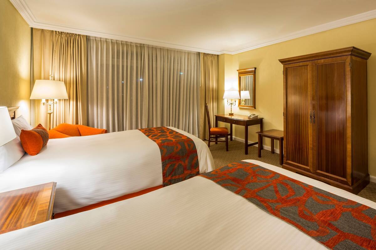 Une chambre d’hôtel avec deux lits, un bureau, une chaise, une armoire et un tableau encadré au mur.