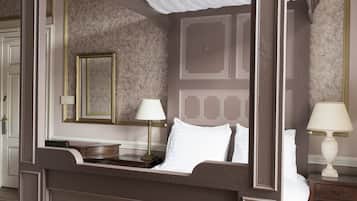 Ein Bett mit Baldachin, ein Nachttisch mit Lampe, ein Spiegel an der Wand und eine Wandtapete mit Muster.