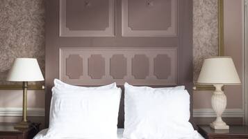 Una cama bien hecha con sábanas blancas y dos lámparas de noche sobre mesitas de madera.