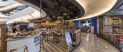 Una cafetería moderna con techo curvo, suelo de madera y diversas opciones de asientos, incluyendo mesas y sillas.