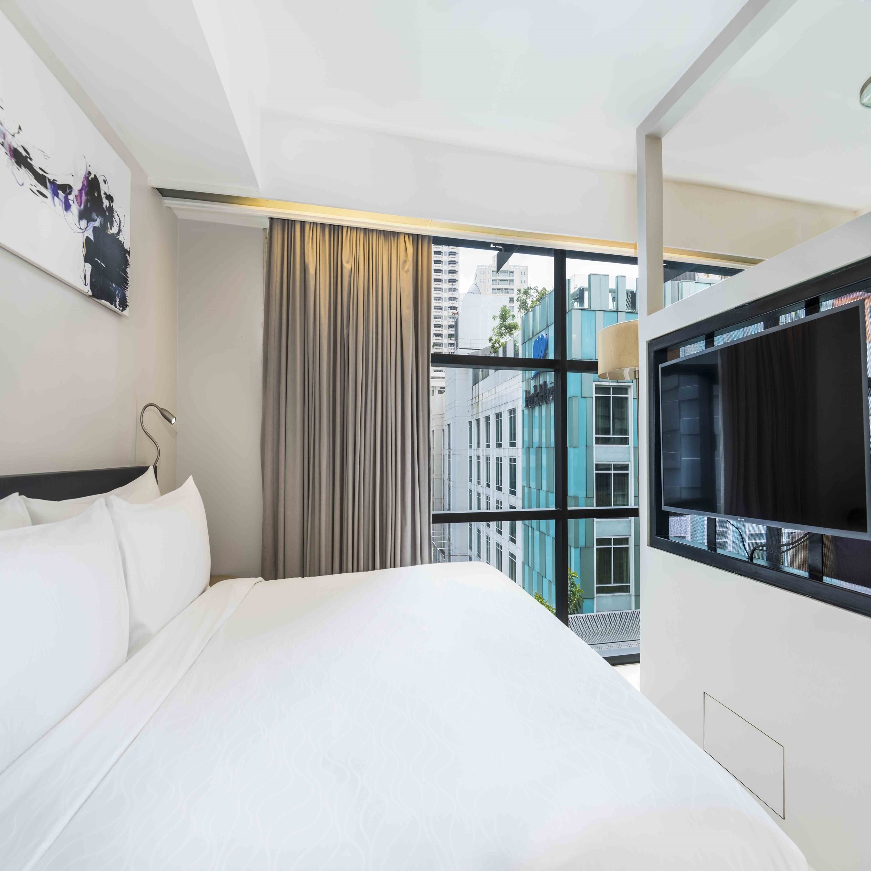 A hotel room with a large bed, a TV, and a view of the cityscape through large windows.
