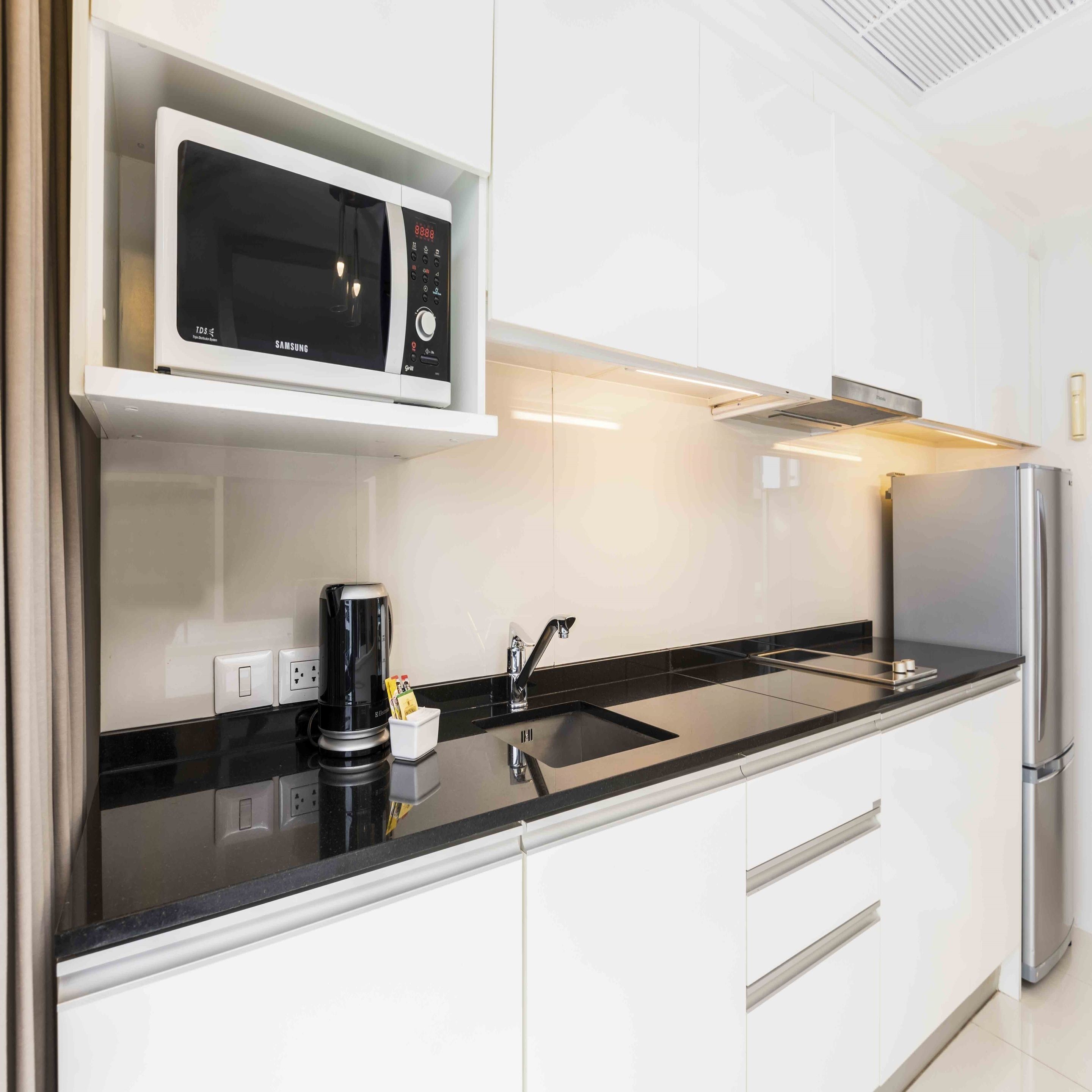 Une cuisine moderne avec des meubles blancs, un plan de travail noir, un réfrigérateur en acier inoxydable, un four à micro-ondes et une machine à café.