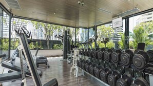 Ein Fitnessstudio mit Trainingsgeräten, Gewichtsständern und großen Fenstern mit Blick auf Gebäude und Grünflächen.