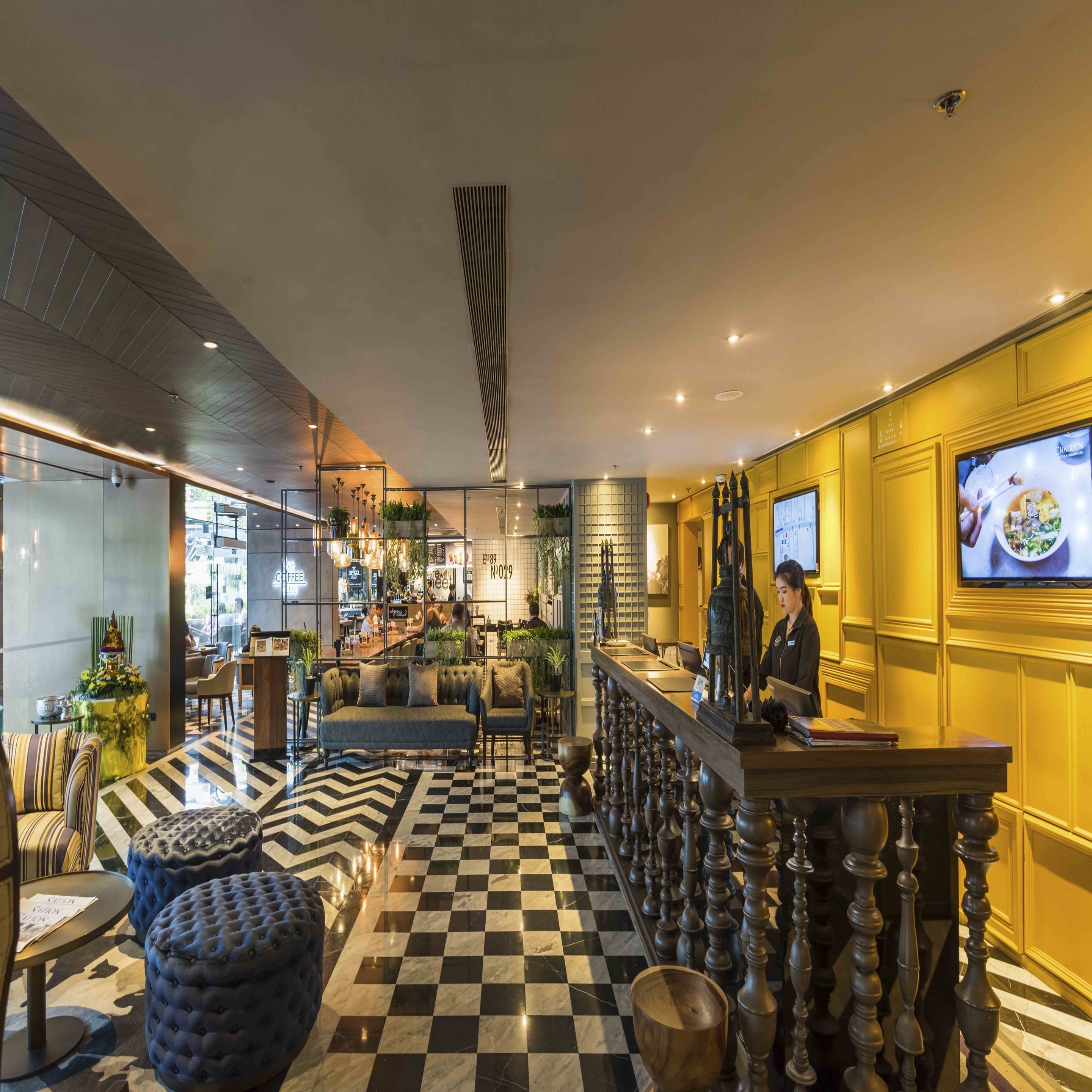 A modern hotel lobby with a checkered floor, seating areas, and a bar.