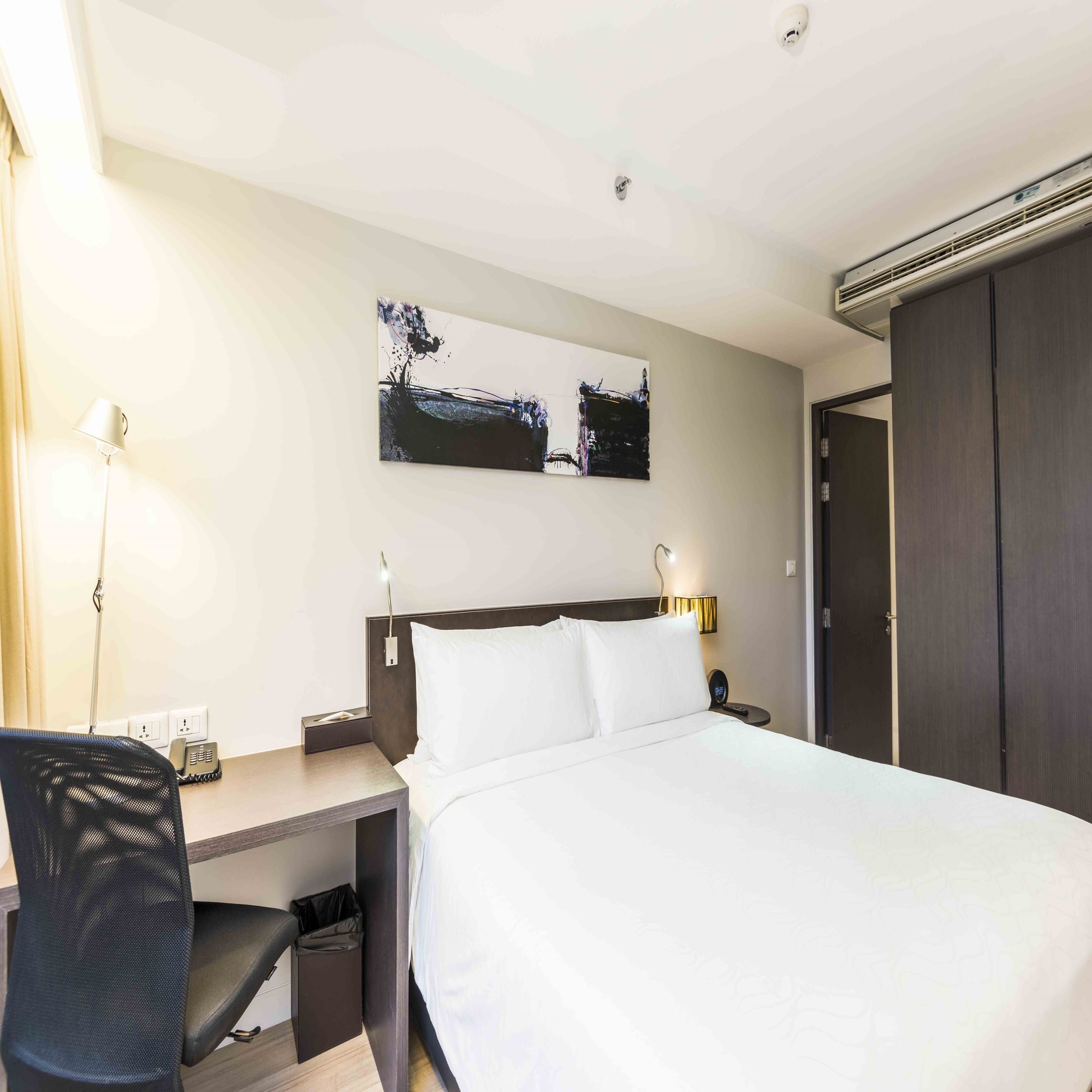 Una habitación de hotel con cama, escritorio, silla y un cuadro en la pared.