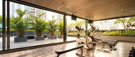 A modern gym with exercise equipment, large windows, and indoor plants.